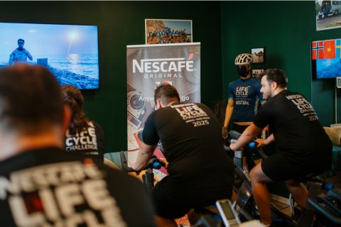 Participants in Nescafe's Life Cycle Challenge ride stationary bikes in a vibrant room decorated with banners