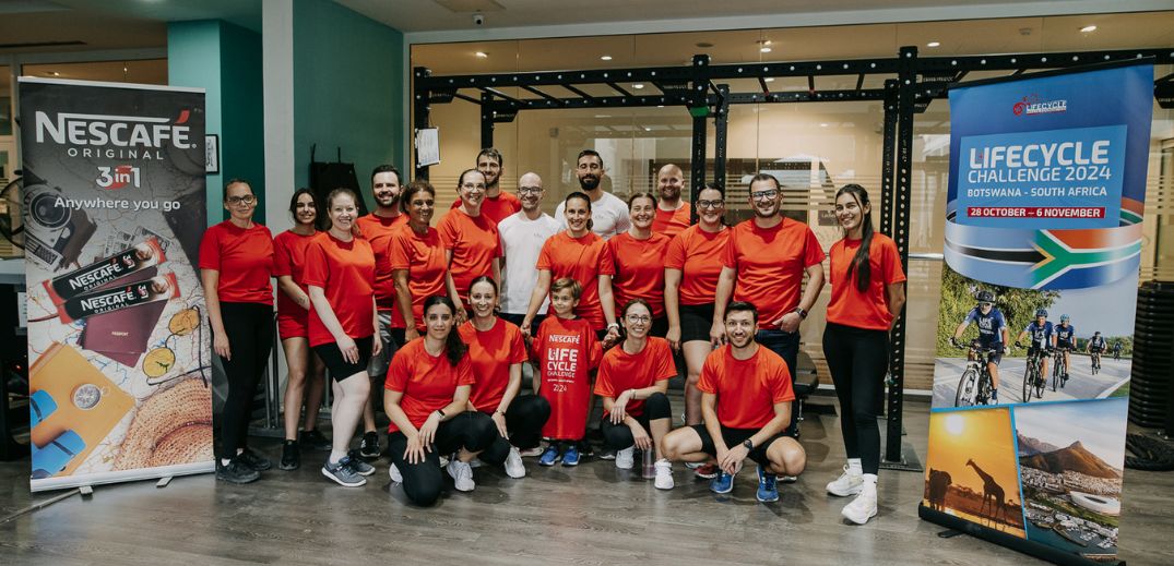 A group of individuals in red shirts poses in front of Nescafé and Lifecycle Challenge banners in a gym setting