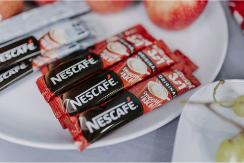 A plate featuring NESCAFÉ instant coffee packets next to fresh apples and grapes, showcasing a cozy snack setting