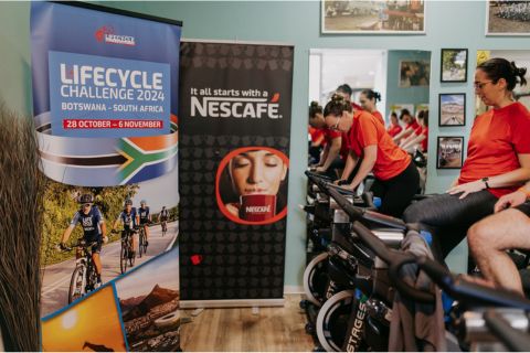 Two promotional banners for the Lifecycle Challenge 2024 in Botswana beside stationary bikes in a fitness studio