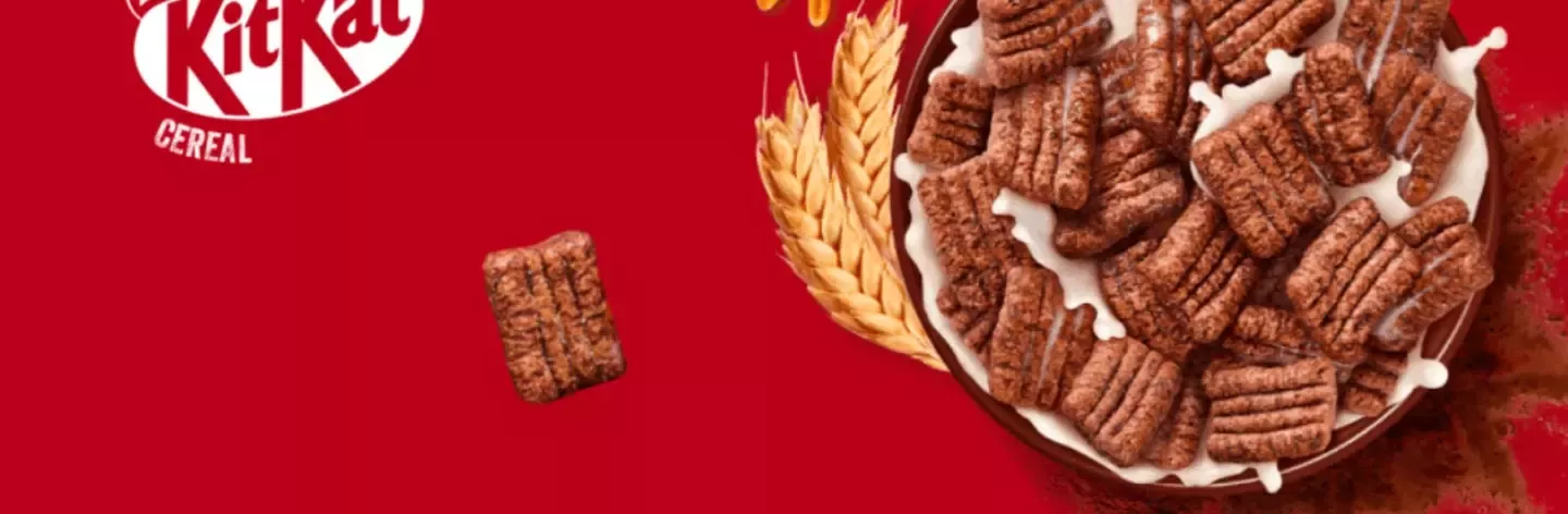 Bowl of KitKat chocolate cereal with milk splashing, wheat stalks, and KitKat logo on red background.