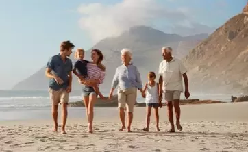 Multigenerational family walking together along a sandy beach with ocean and mountains
