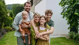 Smiling family with parents, teenagers and a baby standing together in a green garden