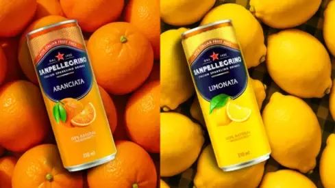 Cans of Sanpellegrino Aranciata and Limonata surrounded by vibrant oranges and lemons on a checkered cloth background