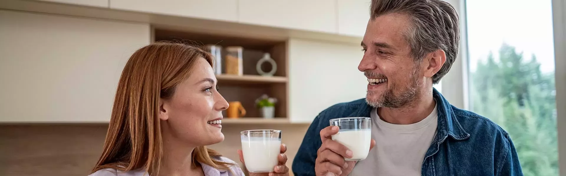 Adult couple holding glasses of milk together in a bright kitchen at home