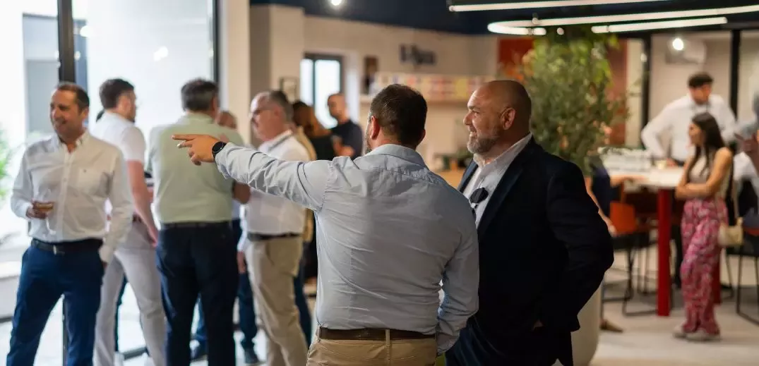 A group of people engage in conversation at a modern, brightly lit venue, with one person gesturing while discussing